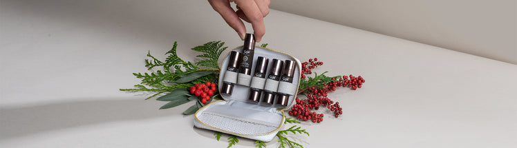 A hand selecting a roll-on from Saje Pocket Farmacy Physical Edition with holiday greenery in the back