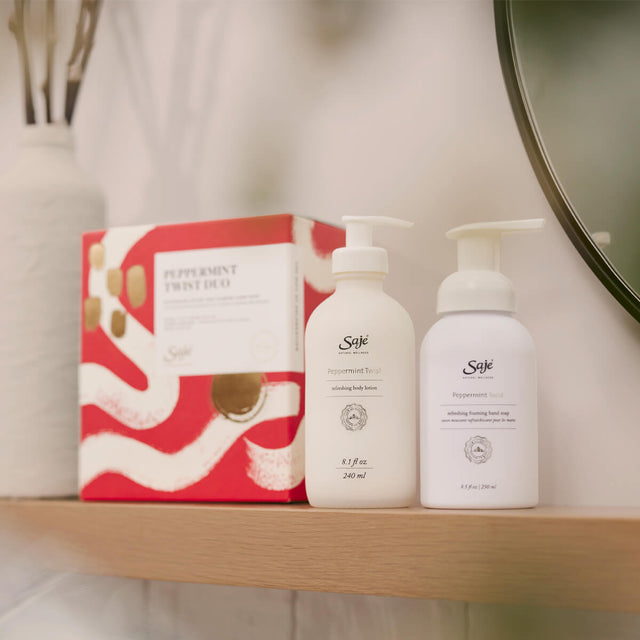 Peppermint twist body lotion and peppermint twist foaming hand soap on a wooden ledge next to a white vase.