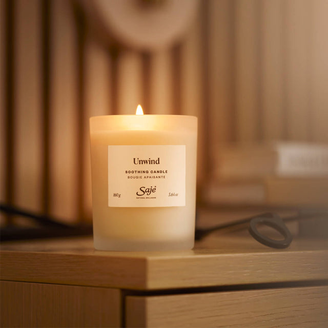 A lit unwind candle sitting on a wooden side table next to a stack of books and a wick trimmer.