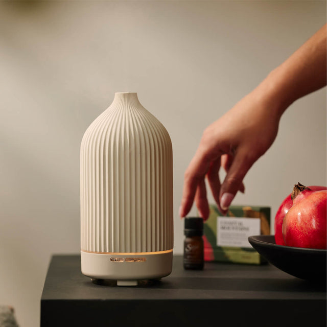 Aroma Rise Cascade Diffuser on a table next to holiday diffuser blend collection and a bowl of pomegranates