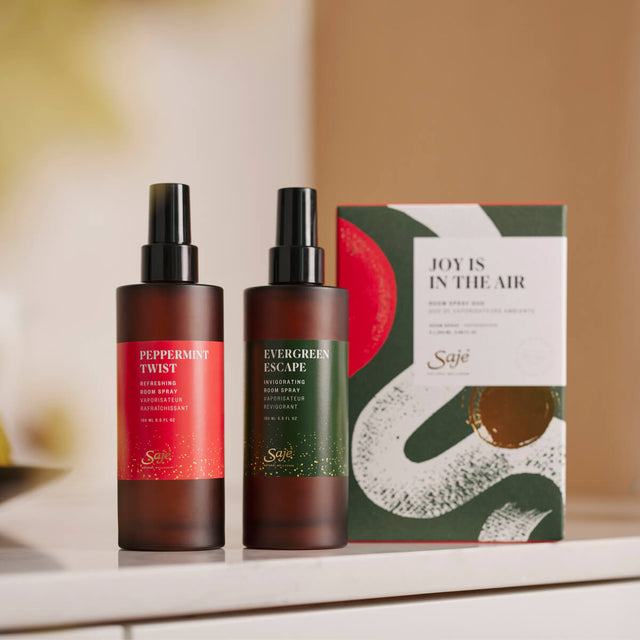 Peppermint twist room spray and evergreen escape room spray next to packaging on a white counter
