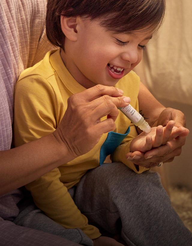 Child giggles while parent applies Aroma Fairy roll-on to child's palm