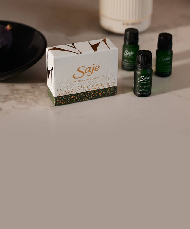 Three seasonal diffuser blends, a holiday blend box, and a decorative bowl of figs are styled on a marble countertop.