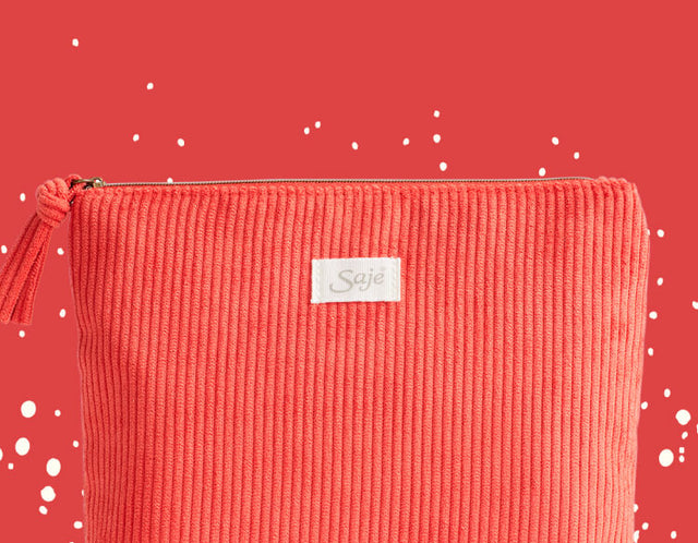 A red corduroy cosmetic bag with tassel zipper detailing against a red background with off-white flecks.