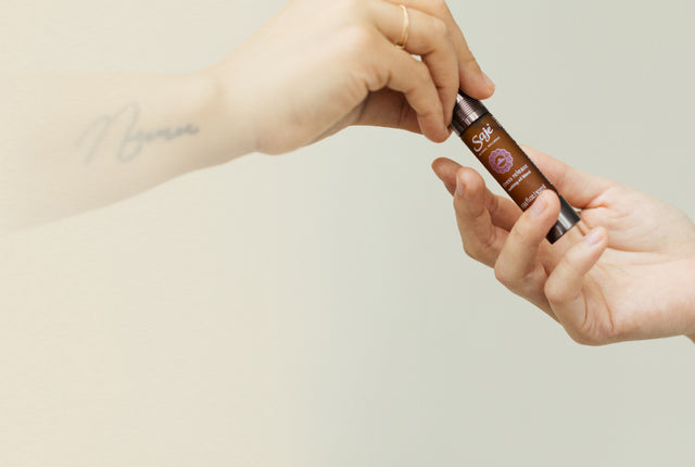 A person hands a Saje remedy roll-on to another person as a gift.