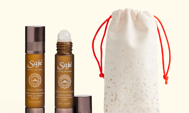 Two Saje roll-ons and a beige canvas holiday bag against a muted yellow background