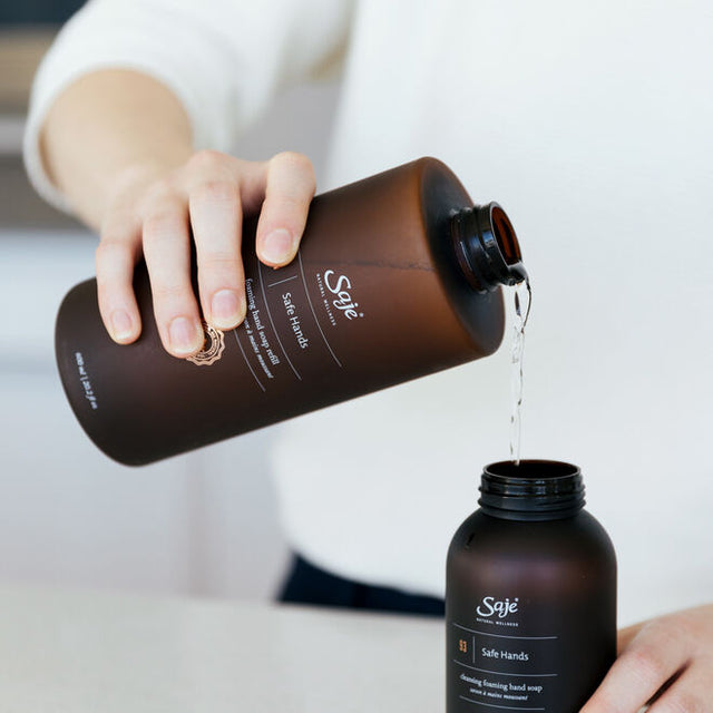 A person refilling their safe hands 250ml bottle of hand soap with the 600ml bottle