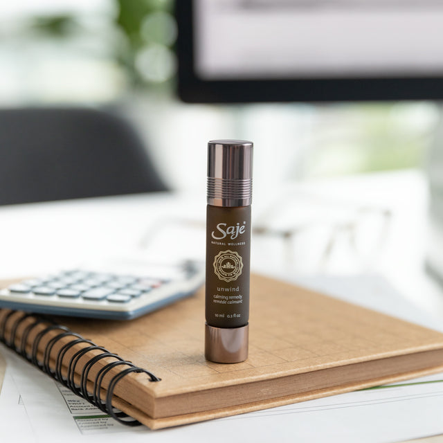 Unwind calming oil blend roll-on placed on top of a notebook