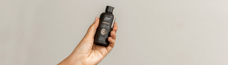 A hand holding a bottle of stress release body oil against a beige background