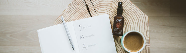 Saje body mist sitting beside a journal and a cup of coffee