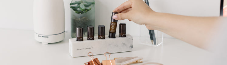 A person choosing a roll-on from Saje Home Farmacy with Aroma Om diffuser in the back
