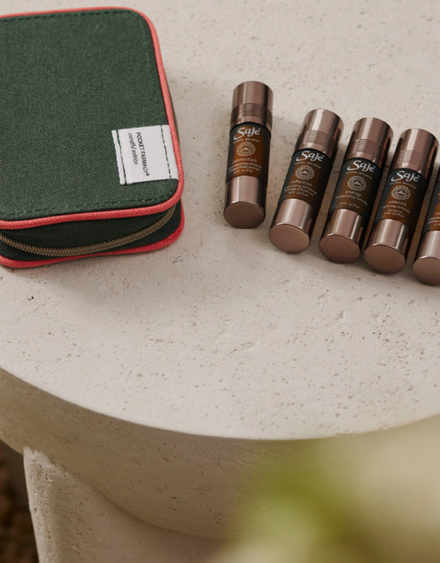 A Saje Pocket Farmacy zipped with five roll-ons next to it placed on a cement side table