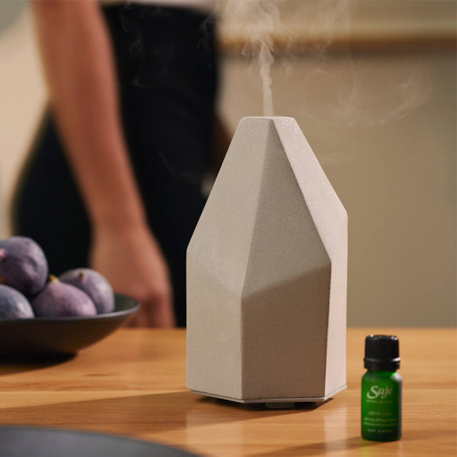 Aroma Elevate diffuser next to a Saje diffuser blend on a counter