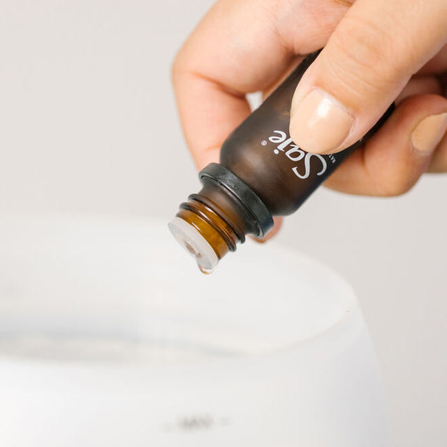 A hand holding a diffuser blend bottle with an oil droplet to go into a diffuser