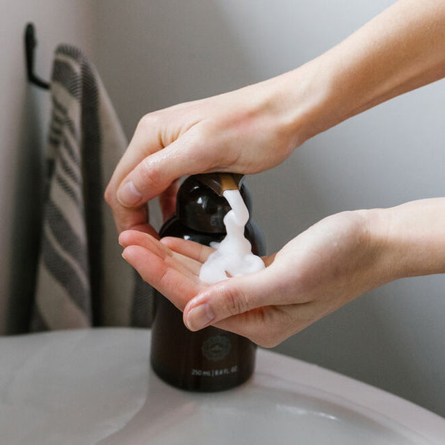 One hand pumping out soap from the dispenser and a hand below being filled with foaming hand soap in a bathroom setting