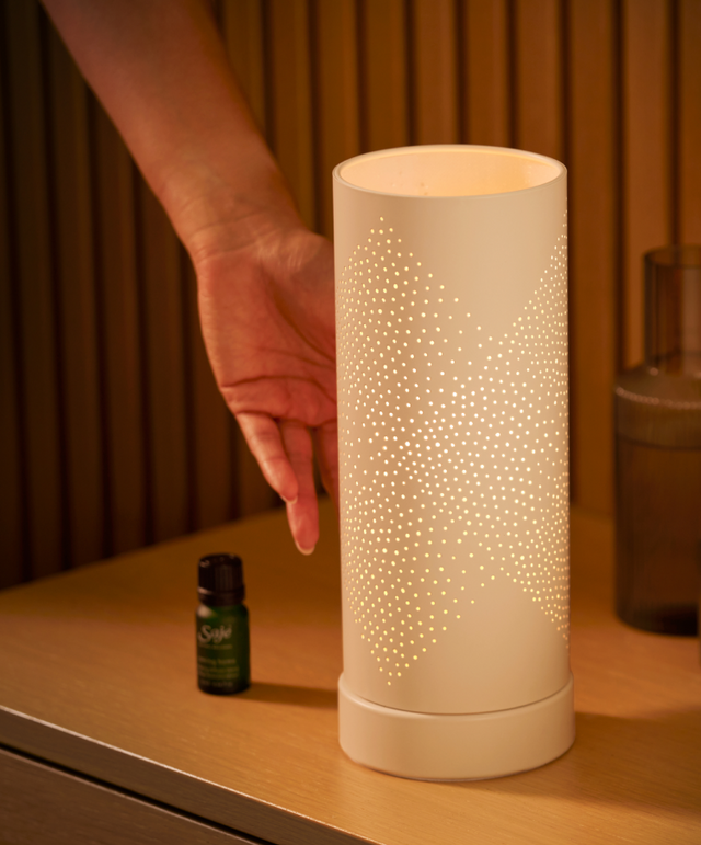 Aroma Light Diamond rests, lit up, on a night stand along with a diffuser blend, water carafe, and catch-all dish.