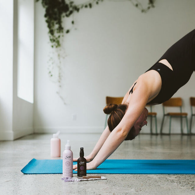 A person on their yoga matt practicing downward dog with their Yoga cleansing mat spray beside them 