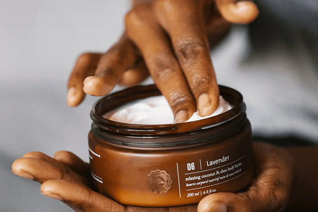 A person holding an opened container of body butter and using their fingers to retrieve product