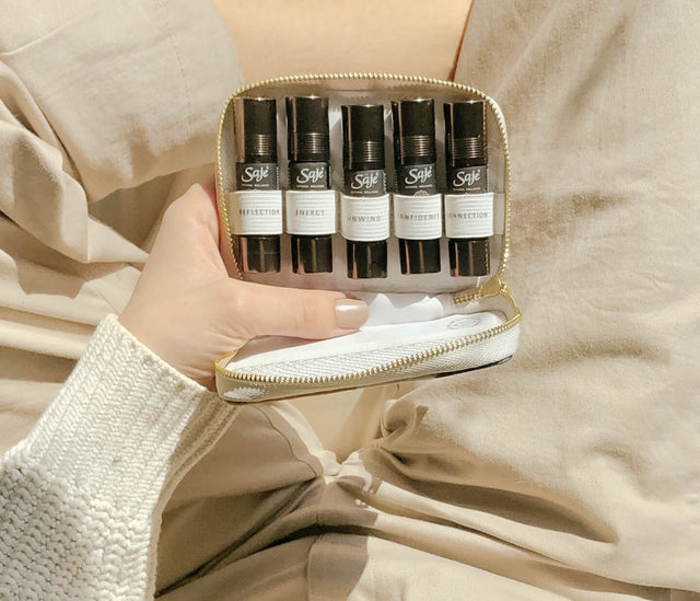 A hand holds five roll-ons showcased in the Mindful Pocket Farmacy kit, against a cream background.