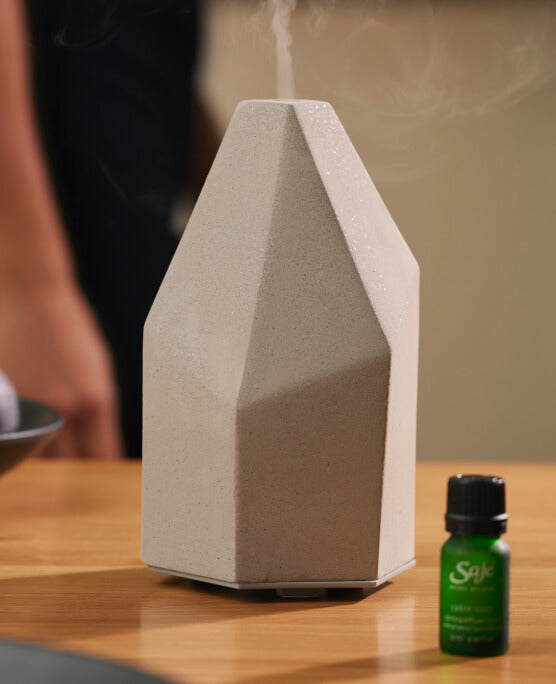 The Aroma Elevate diffuser rests, running, on a wood table. A holiday diffuser blend rests beside it.