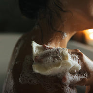 A woman lathers herself in soap in a bathtub.