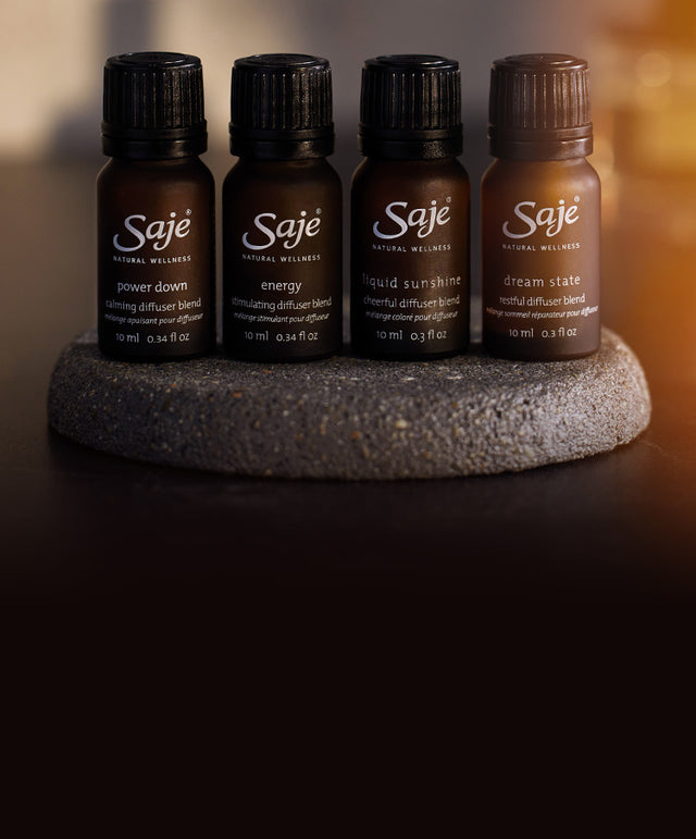 Four small brown-bottled diffuser blends rest on a round grey rock on a countertop.