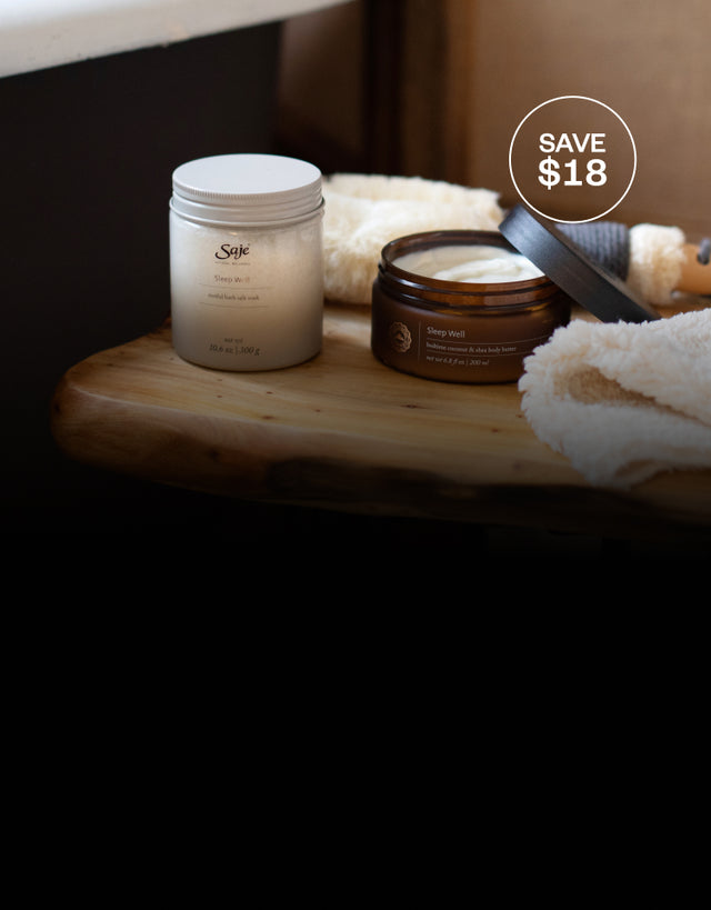 Sleep Well Bath Salt Soak and Body Butter placed on on a wooden stool next to a white wash cloth and dry brush