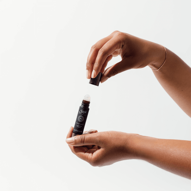 A hand removing the cap off of a Sleep Well oil blend roll-on