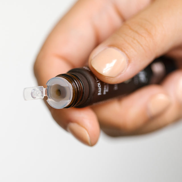 A hand holding a double-ended-blend roll-on bottle, showing that when the cap is removed from the bottom, droplets of the essential oils come out