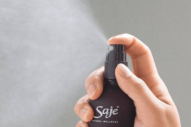 A hand misting a Saje room spray against a grey background