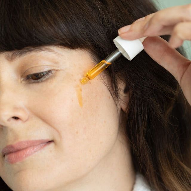 person applying true dew face oil to cheek using the dropper