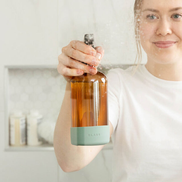 a woman spraying the glass cleaner into the air in a white kitchen