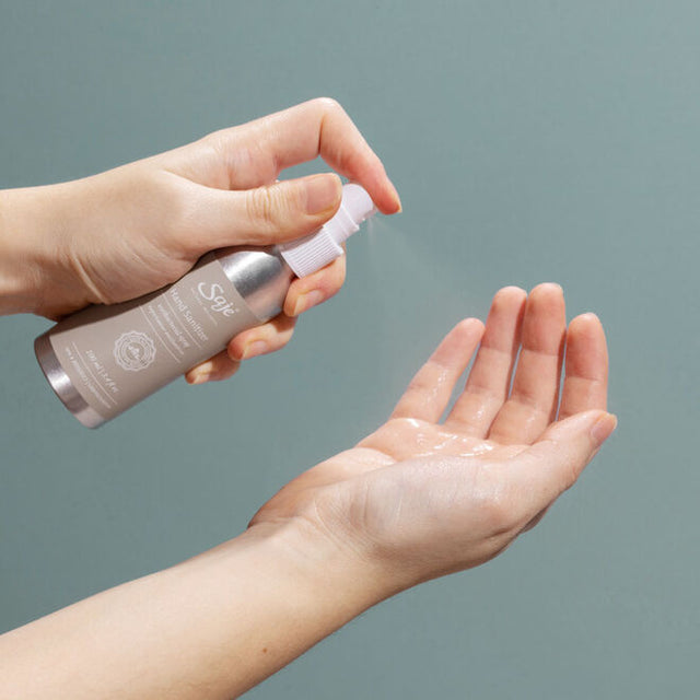 a pair of hands spraying hand sanitizer with a teal background