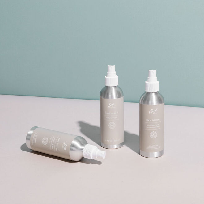 the collection of Saje hand sanitizers on a white counter with a teal background