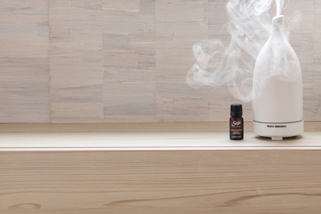 A Saje aroma om diffuser next to a diffuser blend sitting on a wooden ledge