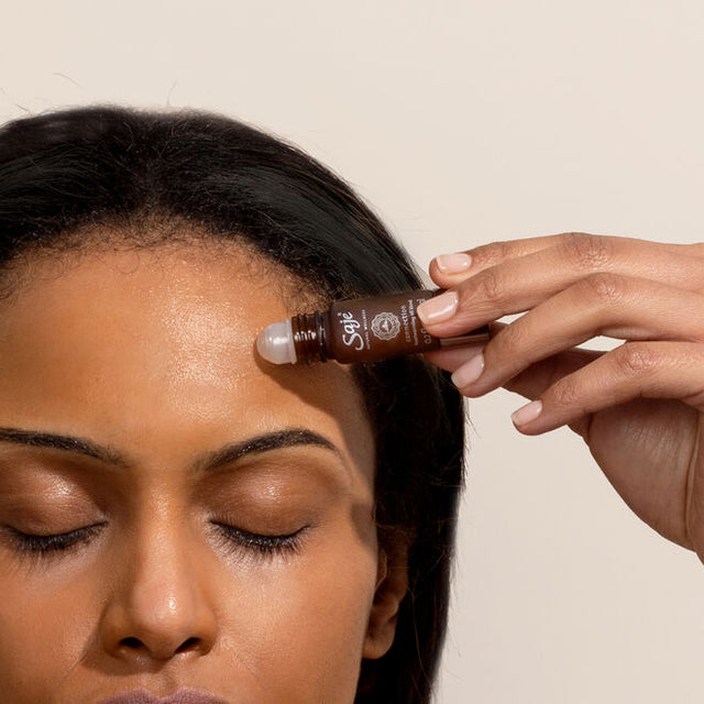 person applying roll-on essential oils on head