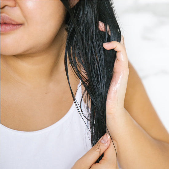 A woman working the Hair repair coconut & argan treatment into the ends of damp hair 