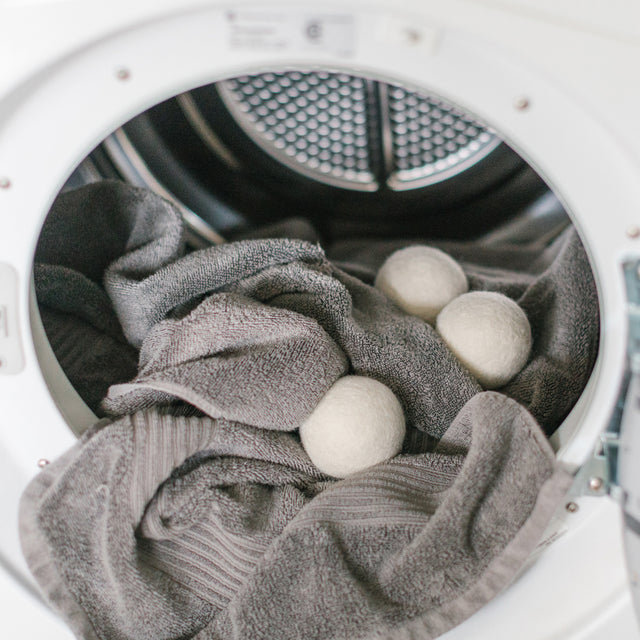 Inside a dryer with charcoal grey towels and three wool laundry balls 