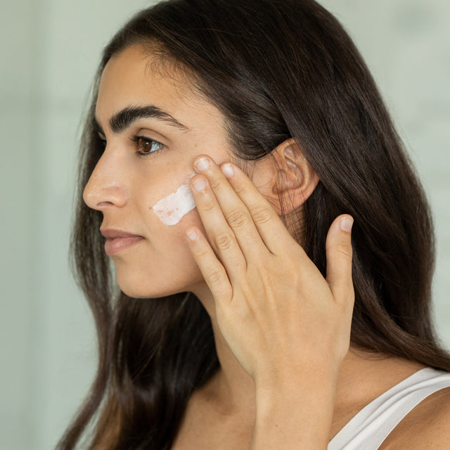 A woman gently massaging Calm-O-Mile Moisturizer in an upwards motion into her skin 