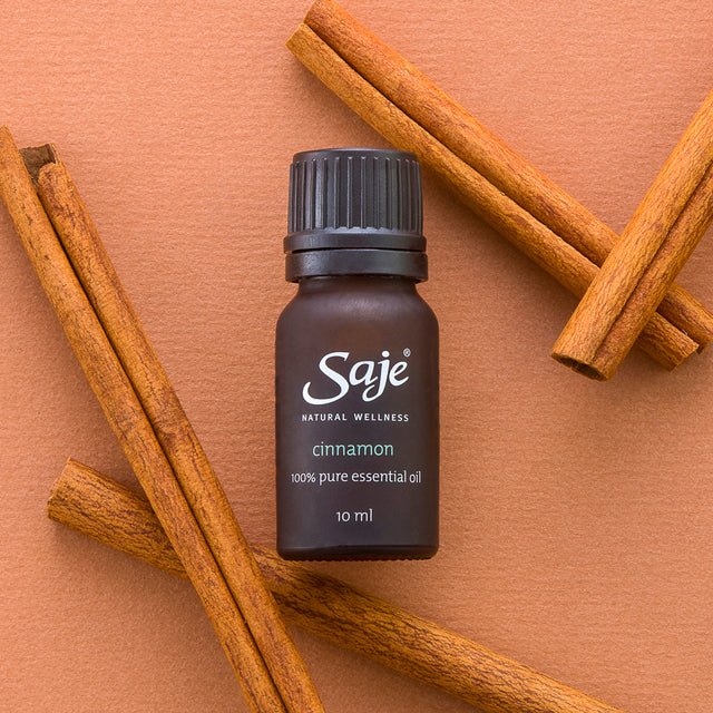 Cinnamon single note essential oil brown bottle with the cap on surrounded by cinnamon sticks on a terracotta background 