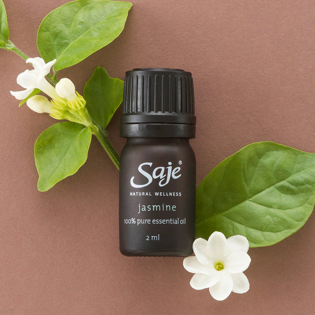 Jasmine essential oil 2ml brown diffuser bottle with the cap on next to jasmine flowers and on a brown background