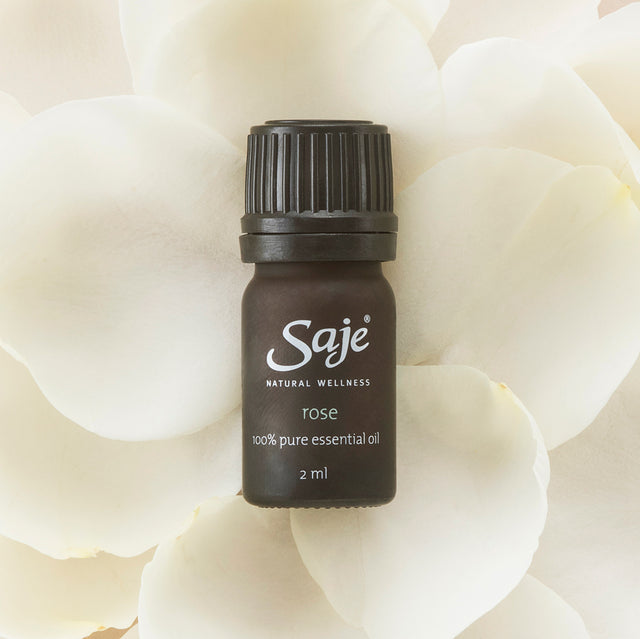 Rose pure essential oil 2ml bottle with cap on on top of white rose pedals