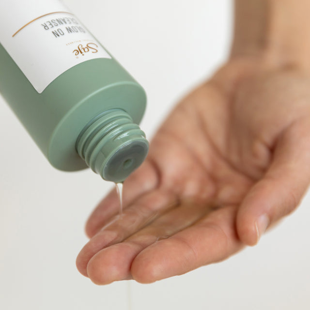 Glow On Cleanser light green bottle with the cap off and the cleanser is being poured into an open hand underneath it