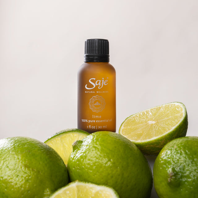 30ml lime essential oil brown bottle with the cap on surrounded by whole limes and slices on a white background
