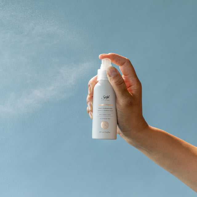 Person spraying deodorant on blue background